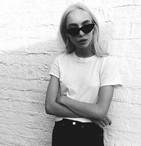Chic black cat eye sunglasses shown on model with minimalist white t-shirt and brick wall