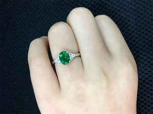 Close-up of vintage emerald ring with side diamonds worn on finger against dark mesh