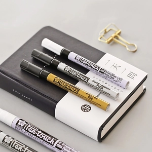 Sakura Pen-touch paint markers in gold, silver, and white on a notebook, 1.0mm and 2.0mm tips