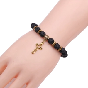Detail of hand wearing yoga bracelet with black lava beads and golden cross charm