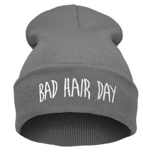 Dettaglio del berretto in maglia grigia con ricamo bianco BAD HAIR DAY su sfondo tinta