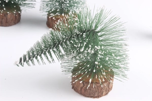 Close-up of mini snow-flocked Christmas trees with wooden bases on white background