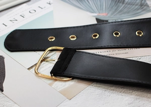 Close-up of black velvet corset belt with golden buckle and eyelets on a stone surface