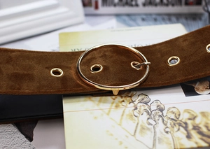 Detail of brown velvet belt featuring a gold round buckle and metallic eyelets