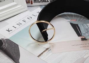 Fashionable black leather waist belt with a large round gold metal buckle on a magazine background