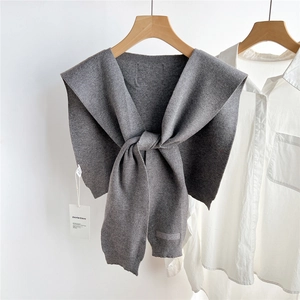 Détail d'un châle tricoté gris avec étiquette de marque et présentation minimaliste