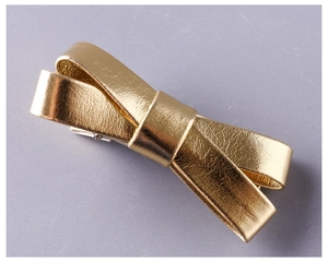 Gedetailleerde close-up van een gouden metallic strik haarklem met getextureerd leer