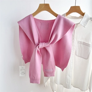 Détail d'un châle tricoté rose avec broderie Doria Dore sur chemise blanche