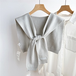 Détail d'un châle en tricot gris clair avec étiquette de marque sur une chemise blanche