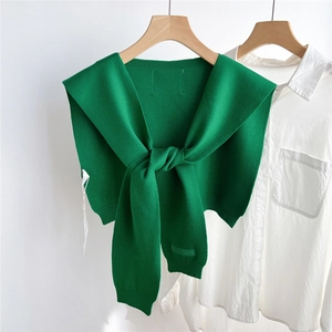 Détail d'un châle tricoté vert avec nœud décoratif sur une chemise blanche