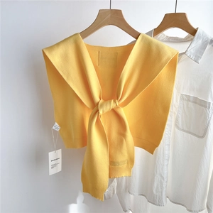 Détail d'un châle en tricot jaune avec nœud frontal et étiquette sur cintre en bois