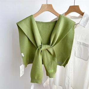 Détail du châle en tricot vert avec nœud élégant et étiquette de marque sur chemise blanche