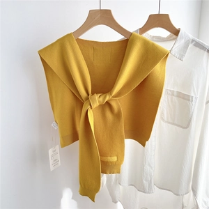 Détail d'un châle en tricot jaune gingembre noué sur une chemise blanche style épuré