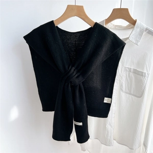 Detail of black knitted wool shawl tied over a white shirt on a wood hanger