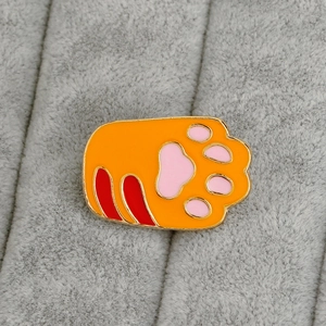 Macro detail of an orange tiger paw enamel brooch with gold trim on gray fabric