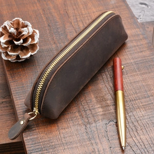 Close-up of a vintage dark brown leather pen case with a golden zipper on a wooden desk