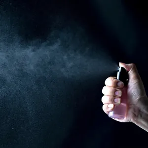 Pink glass spray bottle with black pump head showing fine mist atomization effect