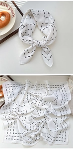Detail of white square scarf featuring black geometric dash patterns and textured fabric