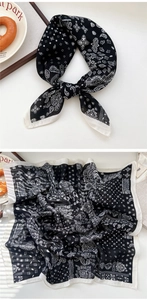 Detail of classic black and white paisley silk scarf tied and draped on white surface