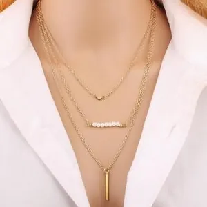 Detail of a three-layer gold necklace featuring pearls and a vertical bar pendant