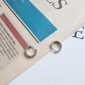 Dettaglio di orecchini a cerchio in argento sterling S925 con marchio su sfondo di giornale