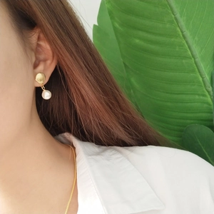 Close-up of model wearing gold shell pearl earrings with white pearl drop detail