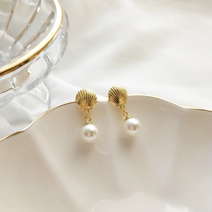 Close-up of gold shell stud earrings with white pearl pendants on elegant white tray