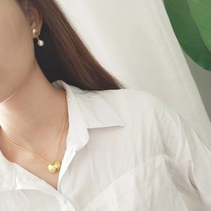 Close-up of model wearing gold shell pendant necklace and matching pearl earrings