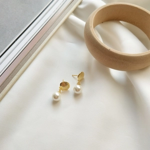 Detailed shot of gold shell stud earrings with white pearls on elegant silk fabric