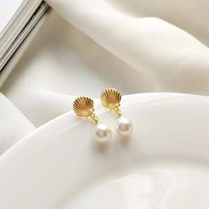 Detail of golden shell-shaped earrings with round pearls on a white porcelain dish