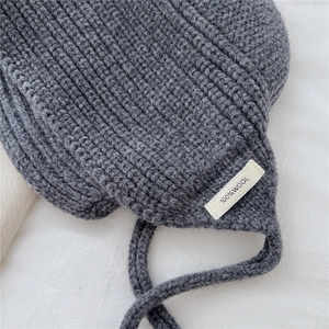 Gros plan du bonnet 100% laine montrant la texture tricotée grise et l'étiquette