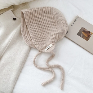Détail d'un bonnet en laine beige avec protège-oreilles et lanières à nouer sur tissu