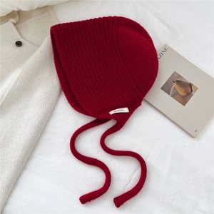 Détail du bonnet en laine rouge foncé 100% avec cordons sur fond de tissu blanc