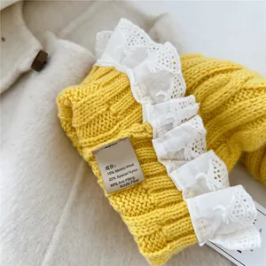 Macro detail of yellow knit scarf with merino wool texture and delicate lace embroidery edge