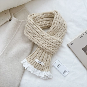 Close-up of beige cable-knit scarf featuring delicate white lace trim and textile brand label