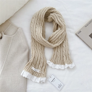 Macro shot of apricot cable knit scarf featuring delicate white lace trim and brand tags