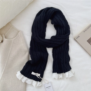 Macro shot of black cable-knit scarf featuring white lace edges and brand tag detailing