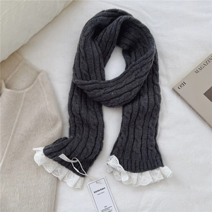 Detail of dark grey cable knit scarf with white lace trim and brand tag on textured fabric