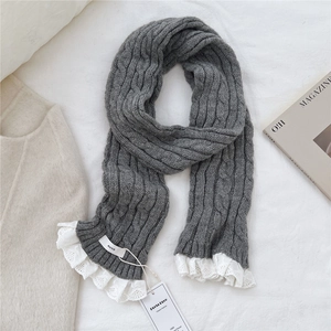 Detail of dark grey cable knit scarf with white lace trim and brand tags on white fabric