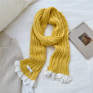Detail of chunky cable knit texture on ginger yellow scarf with delicate white lace trim
