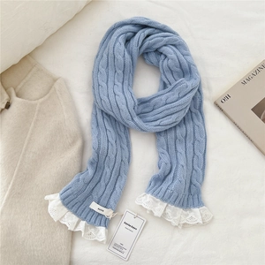 Detail view of light blue cable knit scarf featuring white floral lace trim and logo tag