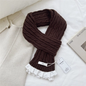 Detail of dark brown cable knit scarf with white lace trim and chic brand label styling