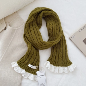 Detail of dark green cable knit scarf featuring white floral lace edges and branded tags