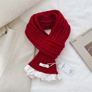 Detail of red cable knit scarf with white lace trim and branded woven label