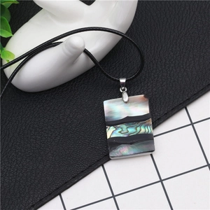 Rectangle abalone shell pendant necklace with rainbow luster and black cord on leather background