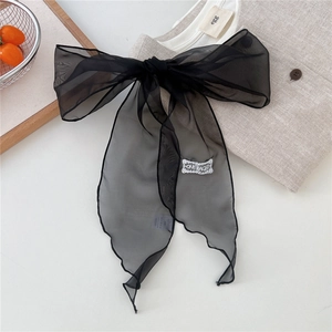 Close-up of black organza bow with white embroidered label on beige knit fabric