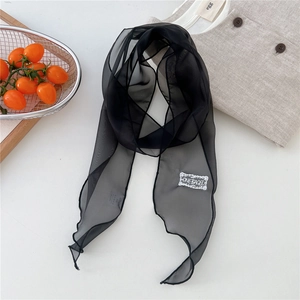 Detail of thin black chiffon scarf with white embroidery and rolled edges on a white desk