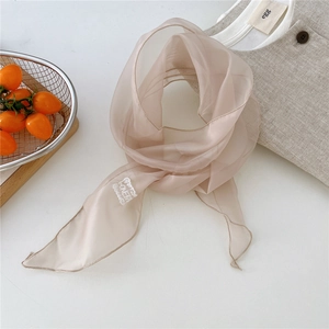 Close-up of lightweight champagne silk scarf with embroidery tag and delicate hem