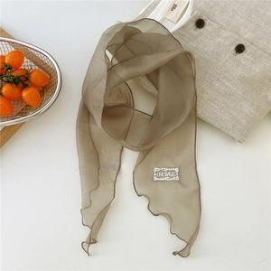 Detail of thin tan silk scarf with embroidered patch and wavy edges on white background