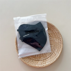 Detail of a black sun protection face mask in branded zipper packaging on a rattan tray